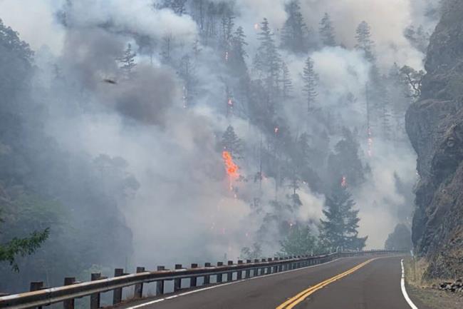FILE - In this photo provided by Caltrans, smoke and flames rise from the Smith River Complex Fire next to the closed U.S. Route 199 in Gasquet, Calif., on Aug. 16, 2023. A Northern California prison was on generator power for a second week and inmates were issued masks to cope with unhealthy air after wildfires knocked out electricity and choked the remote region with smoke. (Caltrans via AP, File)