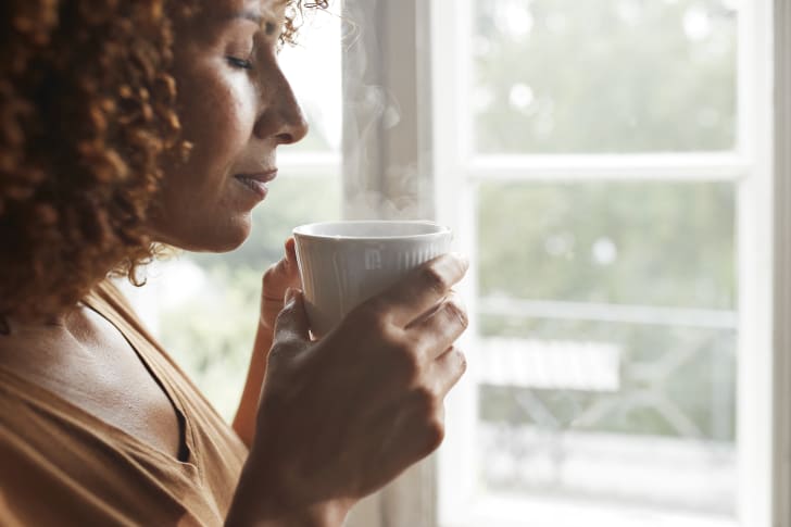 woman sleepily reaching for the snooze button on her alarm clock